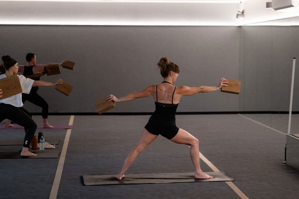 Helen leading Warrior II with a yoga block in each hand